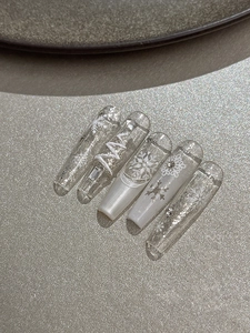 Detail showing long coffin press-on nails with white snowflake prints and silver glitter