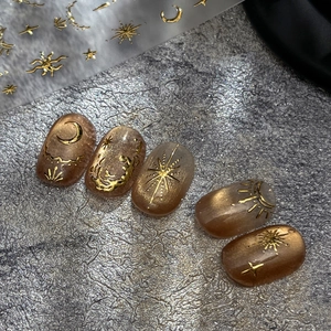 Celestial gold foil nail stickers with star and moon patterns on brown glitter polish
