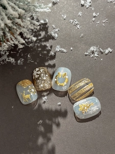 Detail of ice blue Christmas nail art featuring golden reindeer and embossed snowflakes