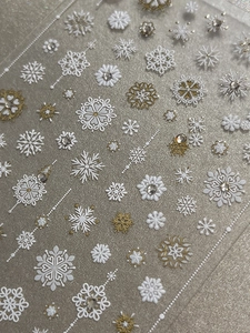 Macro detail of Christmas snowflake nail stickers with gold accents and rhinestones