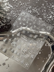 Macro detail of 3D metallic silver Christmas nail stickers with tree and snowflake patterns