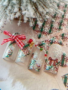 Close-up of Christmas press-on nails with red bow, golden bells, and snowflake patterns