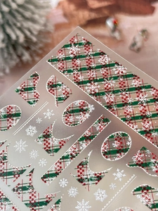 Macro detail of embossed Christmas nail stickers with red green plaid and white snowflakes
