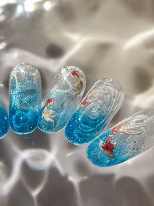 Macro view of blue gradient nail tips with 3D embossed koi fish and glitter detail