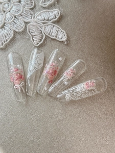 Détail de faux ongles cercueil longs avec roses roses, dentelle et perles blanches