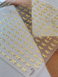Macro detail of 3D embossed golden bow nail stickers with metallic texture on sheet YT6237