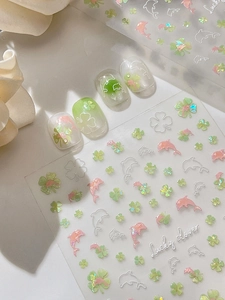 Macro detail of iridescent lucky clover and dolphin nail stickers on natural nails