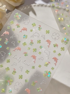 Macro shot of 3D nail stickers featuring pink dolphins, green clovers and aurora laser effect