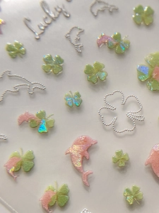 Macro shot of 3D clover and dolphin nail art stickers with laser glitter effect