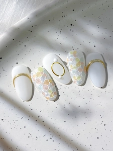 Detailed view of floral press-on nails with pearl accents and gold metal ring decorations