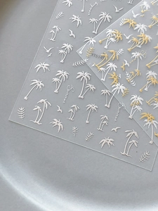 Detail view of summer nail art stickers with palm trees and seagulls in white and gold