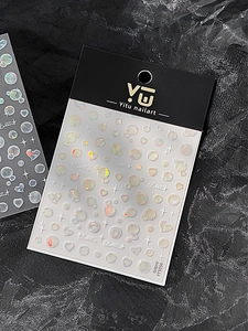 Vue macro de stickers nail art irisés en forme de bulles et coeurs sur surface texturée