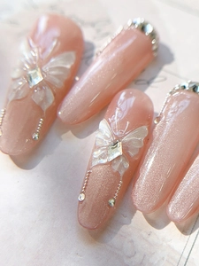 Macro view of nude pink cat-eye press-on nails with 3D white shell butterfly and rhinestones