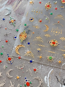 Macro detail of 3D embossed sun and moon nail stickers with metallic gold and silver finish