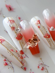 Vue macro de faux ongles fleuris avec noeud 3D, perles et touches de dorure dorée