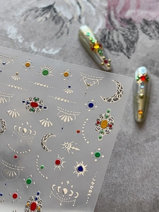 Macro detail of bohemian gold foil nail stickers with sun and moon patterns on grey stone