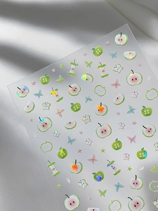 Detailed view of iridescent green apple and butterfly nail art stickers with laser finish