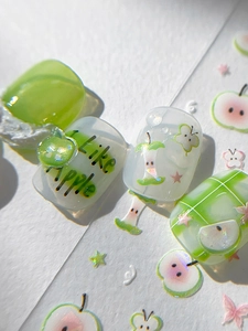 Close-up of green apple press-on nails featuring 3D apple charms and butterfly nail art