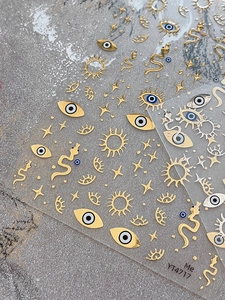 Detailed view of gold foil nail stickers featuring evil eye, sun, and snake patterns