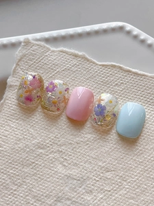 Detailed view of handmade press-on nails with embedded dried flowers and gold silk details