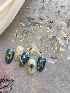 Detail of 3D embossed nail stickers featuring evil eye, snake and star patterns in gold