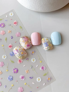 Detailed close-up of floral nail art stickers with daisy patterns and 3D embossed effects