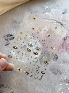 Close-up of gold evil eye nail art stickers featuring stars and snakes YT4717