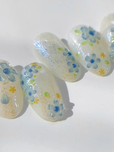 Macro detail of almond nails with blue floral hand-painted art and fine aurora glitter