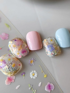 Close-up of floral press-on nails with embedded dried flowers, gold foil, and glitter