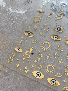 Close-up of gold evil eye and celestial star nail art stickers with metallic finish