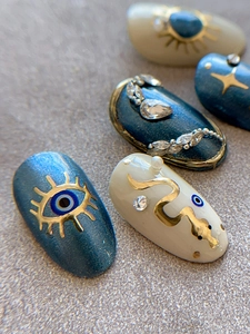 Macro detail of evil eye and gold snake accents on navy blue decorative nail art