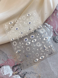 Macro detail of silver foil nail art stickers featuring evil eye and snake motifs