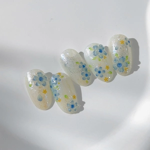 Floral almond press-on nails with blue five-petal flowers and silver glitter finish