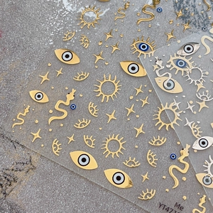 Golden evil eye and star nail stickers with mystic sun and snake patterns on clear film