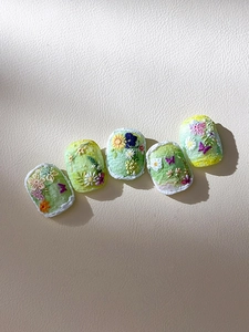Detail showing 3D embossed floral patterns and colorful daisy art on press-on nails