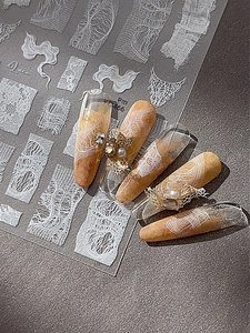 Detailed view of lace nail art stickers with pearls and rhinestones on amber gradient nails