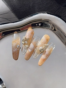 Detail of luxury press-on nails with 3D metal butterfly, pearls, and amber gradients