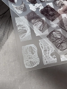 Close-up of black and white lace nail art stickers with delicate mesh and fabric patterns