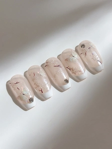 Detail of pink press-on nails with white butterfly patterns and sparkling rhinestones
