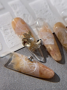 Macro detail of amber nails with white lace, pearls and golden butterfly accents