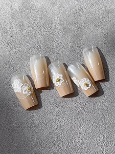 Detail of nude gradient press-on nails with 3D white floral lace and gold beads