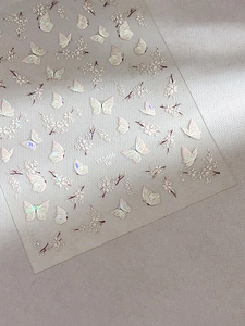 Macro shot of 3D iridescent shell butterfly and floral nail stickers on a grey surface