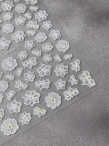 Detailed macro view of 5D white floral embossed nail art stickers on a textured background
