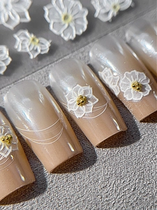 Macro detail of 3D embossed white flowers and gold beads on elegant French ombre nails