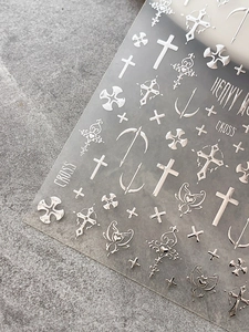 Close-up of gothic silver cross nail art stickers with metallic wing and heart designs
