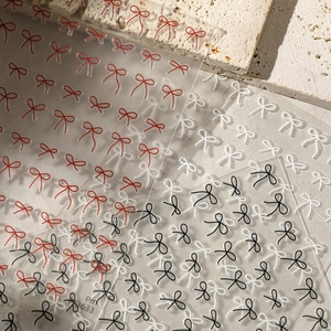 Macro detail of red, black and white bow nail art stickers on a neutral stone background