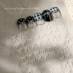Detail view of 3D white bow nail stickers on French style patterned false nails