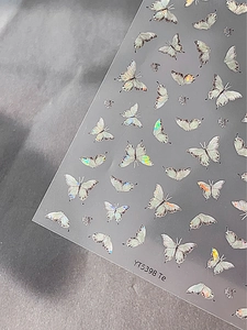 Detailed holographic butterfly nail art stickers with iridescent finish on a grey surface