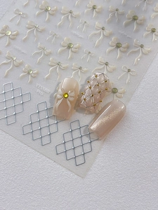 Macro detail of 3D embossed white bow nail stickers with gold rhinestones and silver grid