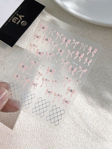 Close-up of pink 3D bow nail art stickers with silver metallic grid patterns on clear film